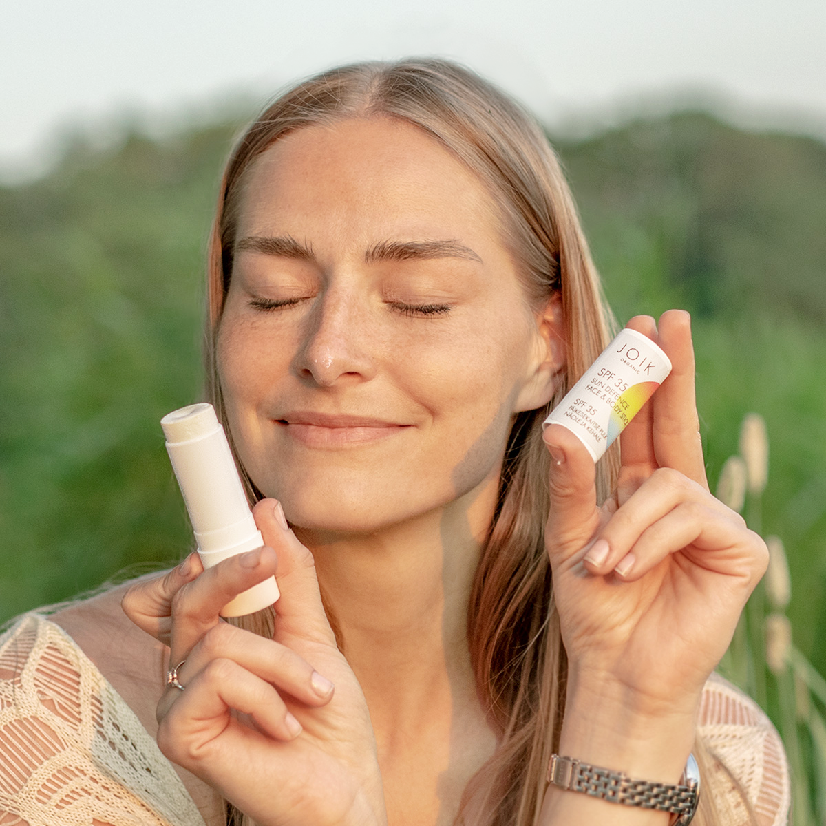 Blonde woman smiling and holding JOIK sunscreen skincare