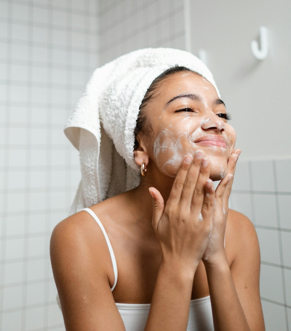 Woman applying skincare in a bathroom with white tiles