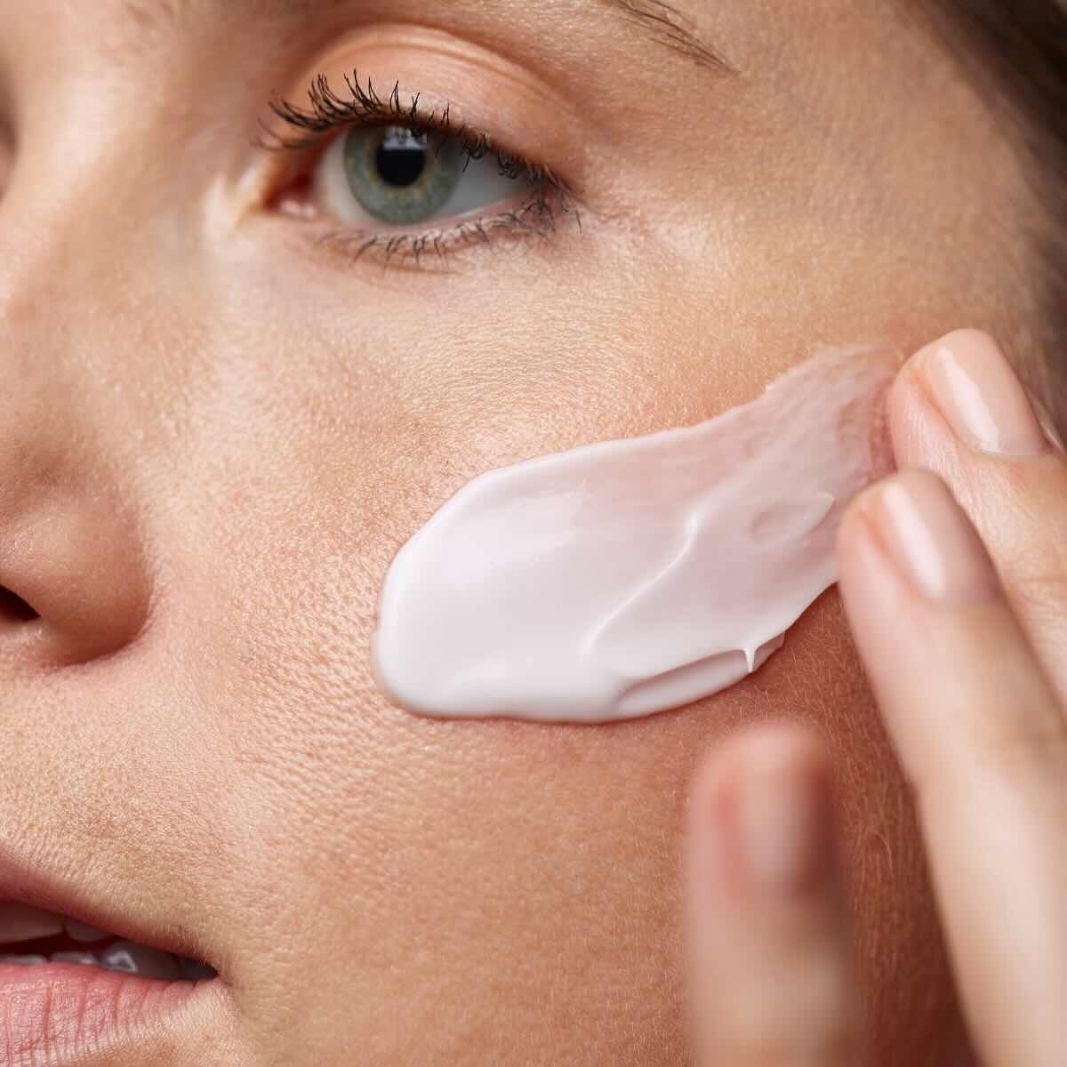 Women spreading skincare creme across left cheek