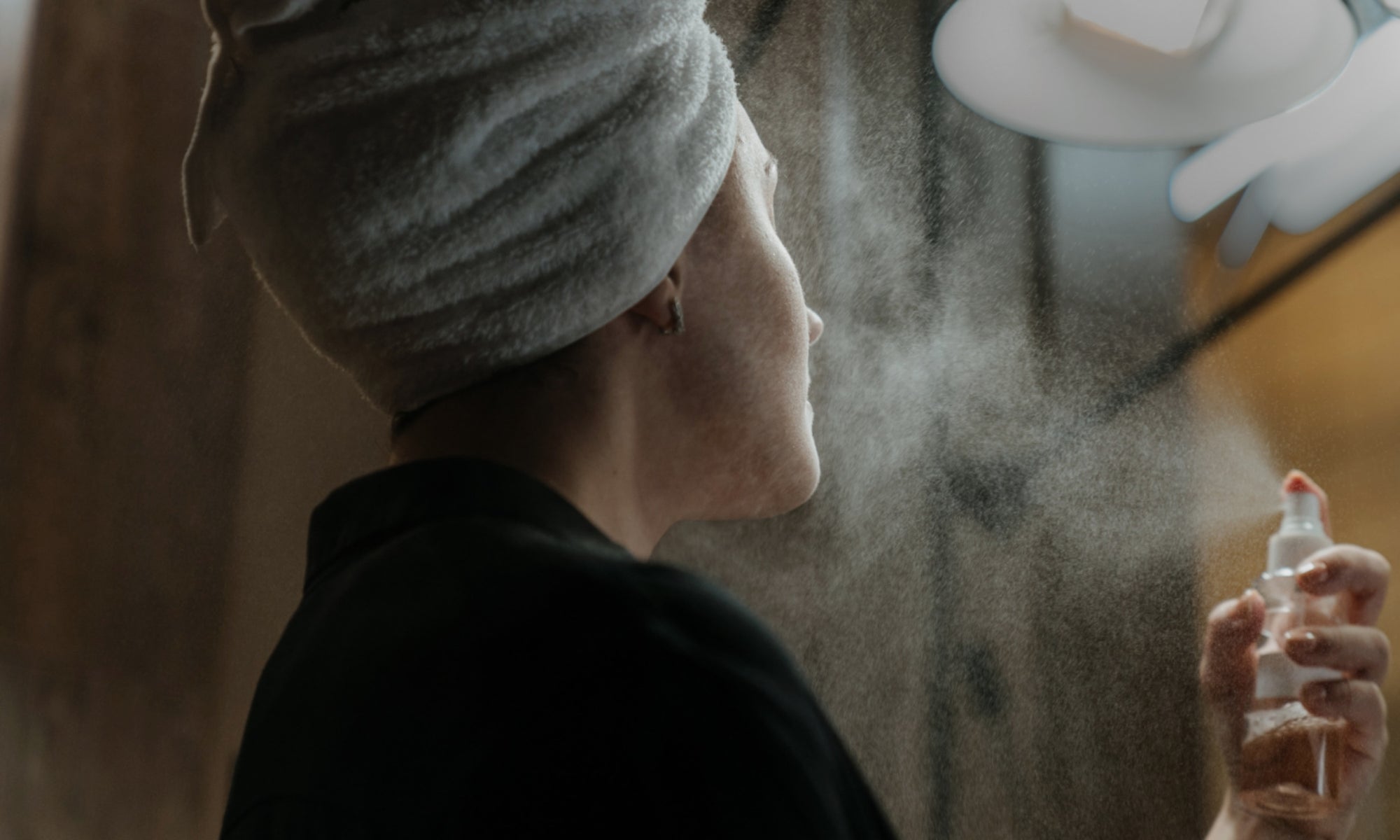 Woman applying skincare product through spray on face
